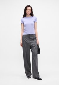 Lyse lilla tætsiddende t-shirt med korte ærmer, parret med højtaljede grå stribede bukser; sort håndtaske, elegante sorte sko.