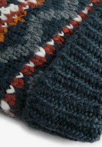 Gestrickte Wurfdecke mit dunkelblauen, grauen, orangefarbenen und weißen Streifen; strukturierte Oberfläche mit dicker Wolle; sichtbare verschlungene Muster.