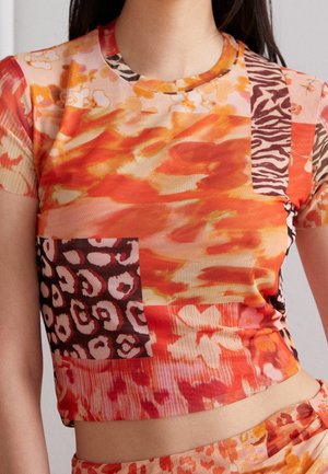Short-sleeve crop top in bright orange and pink, featuring mixed abstract patterns and patches in animal prints and floral designs.