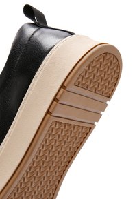 Czarny sneaker z beżową podeszwą i brązową, wzorzystą gumową podeszwą zewnętrzną, uniesiony pod kątem na białym tle.