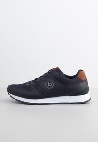 Marinblå träningsskor med en slät yta, bruna läderdetaljer och en vit sula. Har en logotyp och kontrasterande snören.