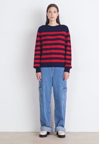 Rot und marineblau gestreifter Pullover mit gerippten Bündchen, kombiniert mit entspannten blauen Jeans-Cargohosen mit Seitentaschen und hochgekrempelten Säumen.