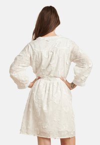 Weißes besticktes Kleid mit langen Ärmeln, tailliertem Schnitt, Blumenmustern und einem leicht gerafften Rock. Leichter, halbtransparenter Stoff.