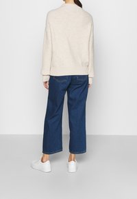 Pull beige en maille avec un large ourlet côtelé, associé à un jean en denim bleu à coupe ample et des baskets blanches. Design simple et décontracté.