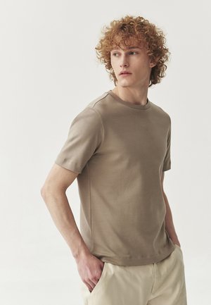 Helles braunes T-Shirt mit kurzen Ärmeln aus weichem Stoff, mit Rundhalsausschnitt und nahtlosem Schulterdesign, kombiniert mit beigen Hosen.