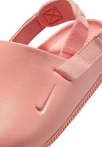 Sandale Nike en matériau rose doux, avec une sangle texturée et un corps de chaussure lisse. Présente une forme incurvée et un détail de logo subtil.