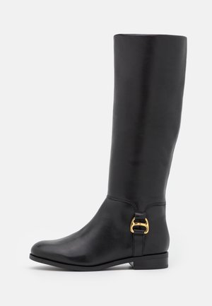 Botte en cuir noire montant jusqu'au genou avec petit talon et détail de boucle dorée près de la cheville, finition lisse, vue de côté sur fond blanc.