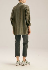 Przesadnie duża zielono-czarna koszula w kratę, zestawiona z ciemnoszarymi dżinsami i białymi trampkami z zielonymi akcentami, widziana z tyłu.