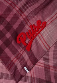 Tissu à carreaux rouge et rose avec une broderie rouge texturée "Pulse" et une petite étiquette blanche indiquant "Cecil" dans le coin.