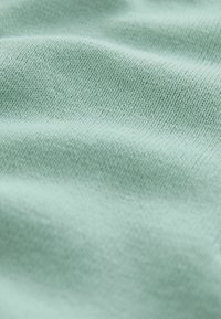 Tissu vert clair avec une finition lisse et texturée. Le tissage est serré et homogène, mettant en valeur sa douceur.