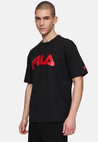 Sort kortærmet T-shirt lavet af bomuld med et stort rødt FILA-logo på forsiden og et mindre logo på den højre ærme.