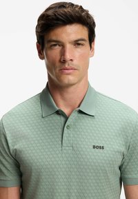 Polo verde claro con un patrón hexagonal texturizado, cuello y mangas cortas, con el logo "BOSS" bordado en el pecho.