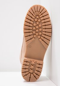 Sula av ljusbrun känga med stjärnformade mönster och storleksnummer 37, placerad stående mot ett vitt hörn.