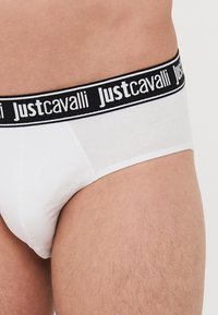 Beli bombaži hlačke z črnim elastičnim pasom, na katerem je v belem natiskan logo "Justcavalli". Gladka tekstura in standardna prileganje.