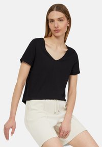 Czarny bawełniany t-shirt z krótkim rękawem i dekoltem w serek z podwiniętymi rękawami, w zestawie z jasnobeżowymi szortami dresowymi z elastycznym pasem i sznurkiem.