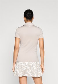 Πολό πshirt σε ανοιχτό μπεζ με ριγωτό γιακά και κοντά μανίκια, σε συνδυασμό με φούστα λευκού χρώματος με σχέδιο. Λείος υφασματικός σχεδιασμός, εφαρμόστης γραμμή.