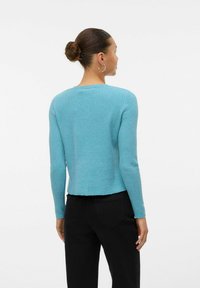 Haut à manches longues côtelé bleu clair avec un col arrondi et un ourlet court. Présente un tissu texturé et une silhouette ajustée.
