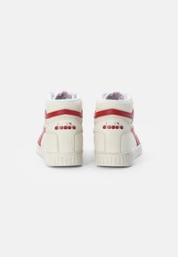 High-top sneakers in cream leather with red accents and textured rubber soles. Features padded collar and logo on the side.