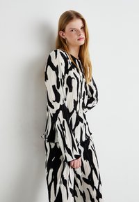 Ensemble haut et jupe en noir et blanc à motifs abstraits, à manches longues et coupe décontractée. Texture lisse et design fluide.