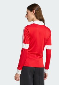 Rød langermet skjorte med hvit krage og hvite akcentstriper på ermene. Mykt stoff med jevn tekstur, fitted design.