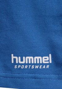 Blå sporttøy-stoff med ribbet tekstur, med "hummel" och "SPORTSWEAR" tryckt i vitt vid nederkanten.
