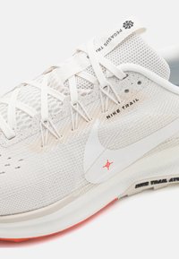 Nike Trail running shoe featuring a lightweight, cream mesh upper, white accents, and a textured rubber sole with an orange highlight.
