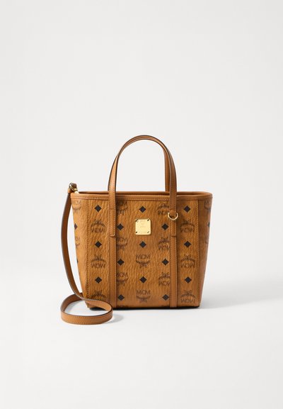 Medium brown leather tote bag with black MCM logo patterns, two handles, a long strap, and a gold square brand plaque on the front.