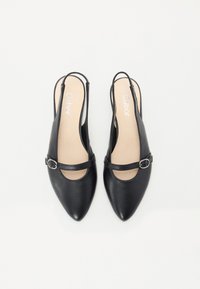 Chaussures slingback en cuir noir avec des orteils pointus, des découpes ajourées et une sangle étroite avec une petite boucle en métal. Texture lisse.