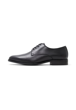 Zapato de vestir negro de cuero con una forma estilizada, diseño minimalista, cuatro ojales para los cordones y un tacón bajo y plano. Textura suave.