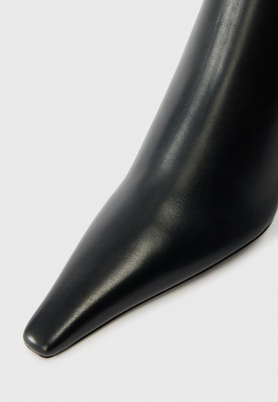 Zapato de tacón alto de cuero negro con punta afilada y textura suave, con un diseño elegante y aerodinámico.