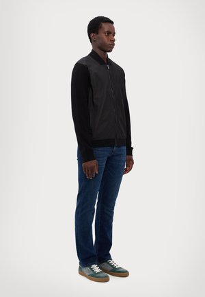 Svart bomberjacka med läderfront, stickade ärmar, dragkedja. Bärs med blå jeans och gröna sneakers med vita snören.