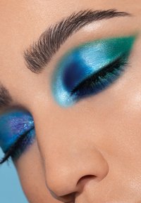 Sombra de ojos azul brillante y verde con acabados brillantes, que presenta degradados y brillos, aplicada sobre los párpados, con cejas cuidadosamente arregladas.