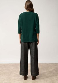 Maglione in maglia tessuta verde scuro con maniche a tre quarti, abbinato a pantaloni in denim scuri a vita alta e a gamba larga con cuciture a contrasto.