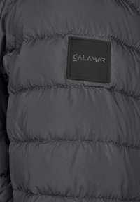 Pufferjakke i mørkegrå stof med quiltet design. Har et tekstureret sort mærke med "CALAMAR" præget i sølv.
