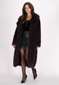 Lang bordeaux faux fur frakke med brede krave, båret over en sort top og lædernederdel. Sorte høje hæle fuldender looket.