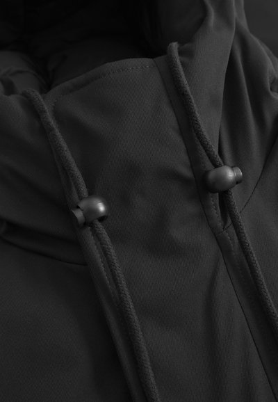 Black jacket with a textured fabric, featuring a hood and drawstrings secured by black plastic toggles. Close-up view highlighting details.