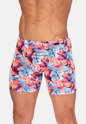 Männlicher Oberkörper mit eng anliegenden, farbenfrohen Badeshorts mit einem lebhaften Blumenmuster in Blau-, Pink-, Orange- und Lilatönen.