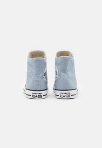 High-top canvas sneakers in light blue with white stitching, black rubber sole, and a circular logo patch on each side.