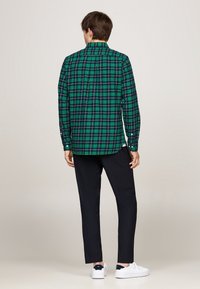 Groen en zwart geruite overhemd, lange mouwen, knoopsluiting kraag en een recht gesneden achterkant. Gecombineerd met donkere broeken en witte sneakers.