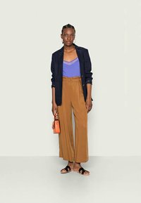 Blazer azul-marinho, top de alça lavanda, calças largas castanhas, sandálias pretas e uma bolsa laranja. Texturas suaves e corte descontraído.