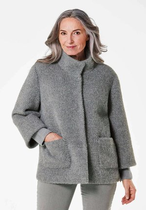 Veste en tricot gris texturé avec un col haut, deux poches avant et des poignets côtelés. Coupe ample et tissu doux.