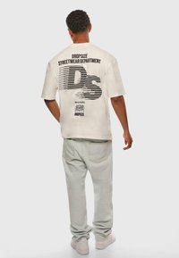 Light beige oversized t-shirt with black graphic text on the back. Pair of light green denim jeans and white sneakers.