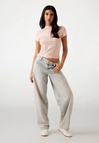 Lyserød top med korte ærmer og teksturdetaljer, kombineret med løstsiddende, lyseblå denimjeans og hvide sneakers.