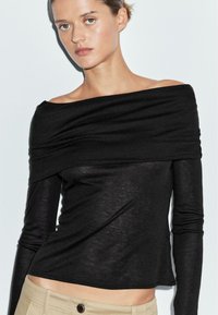 Black, long-sleeved top with off-the-shoulder design, made from lightweight, textured fabric; fitted shape with gathered detail at the neckline.