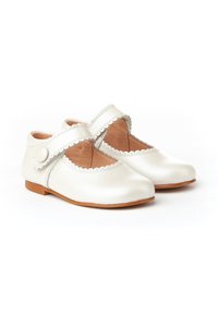 Zapatos Mary Jane de cuero blanco con bordes en forma de onda, puntera redonda, correa decorativa y un pequeño botón como acento. Suelas de color marrón claro.