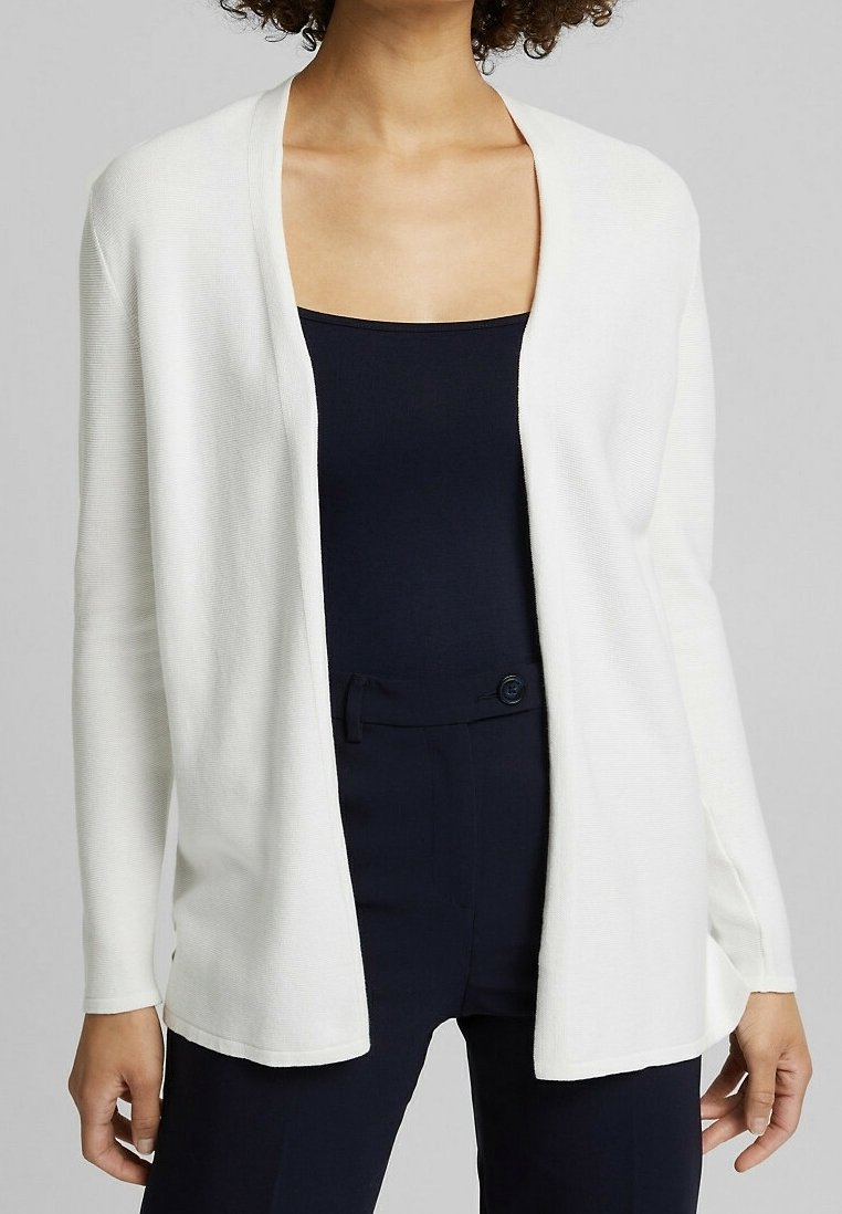 Bílý kardigan s otevřeným předním zapínáním, dlouhými rukávy, texturovaným pleteným materiálem a volným střihem. Nositý přes námořnický top a kalhoty.
