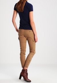 Marinblå kortärmad pikétröja kombinerad med tanfärgade slim fit cargo-byxor med sidofickor och dragkedjor, kompletterat med bruna ankelstövlar.