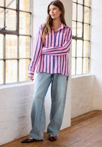 Striped pink and navy shirt with buttons and a chest pocket, paired with light blue wide-leg jeans and dark brown pointed-toe shoes.