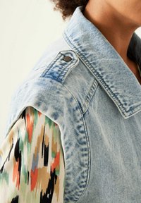 Jeansjacka med blåtvättad front, med ett mönstrat flerfärgat tyg på ärmarna. Inkluderar en tryckknappdetalj på axeln.