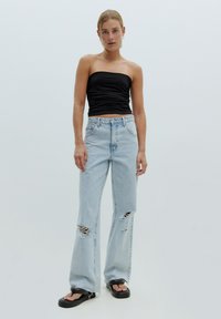 Zwarte strapless top, lichtblauwe high-waisted jeans met versleten details, en zwarte platform sandalen. Glad materiaal en een comfortabele pasvorm.
